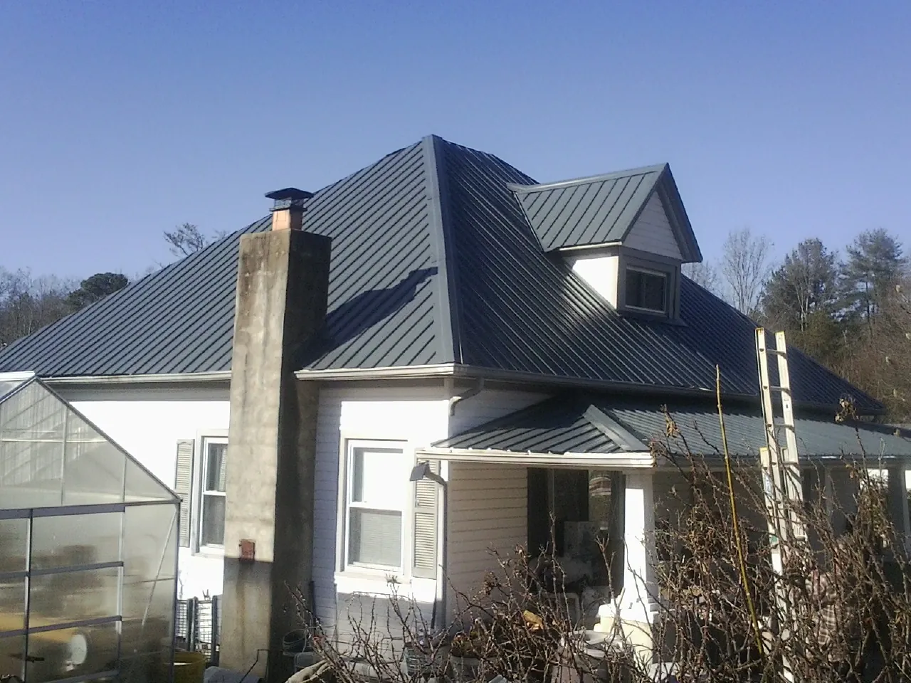 Dark blue standing seam metal roof on a white farmhouse with dormer — Slate & Tile Roof Repair by Roofing Brothers in Eminence