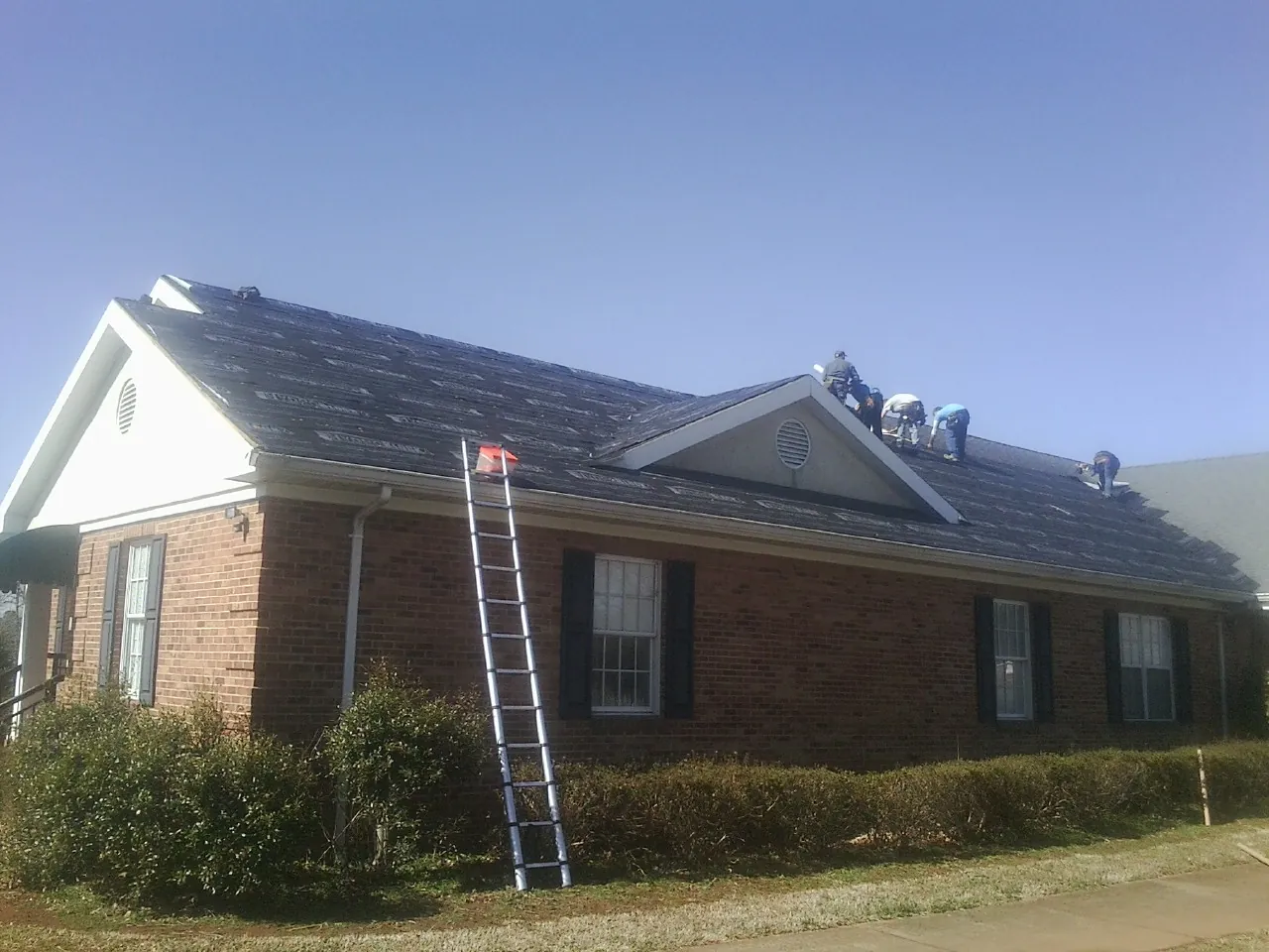 Crew tearing shingles off a brick ranch roof with a ladder set — Emergency Roof Repair work by our crew in Eminence