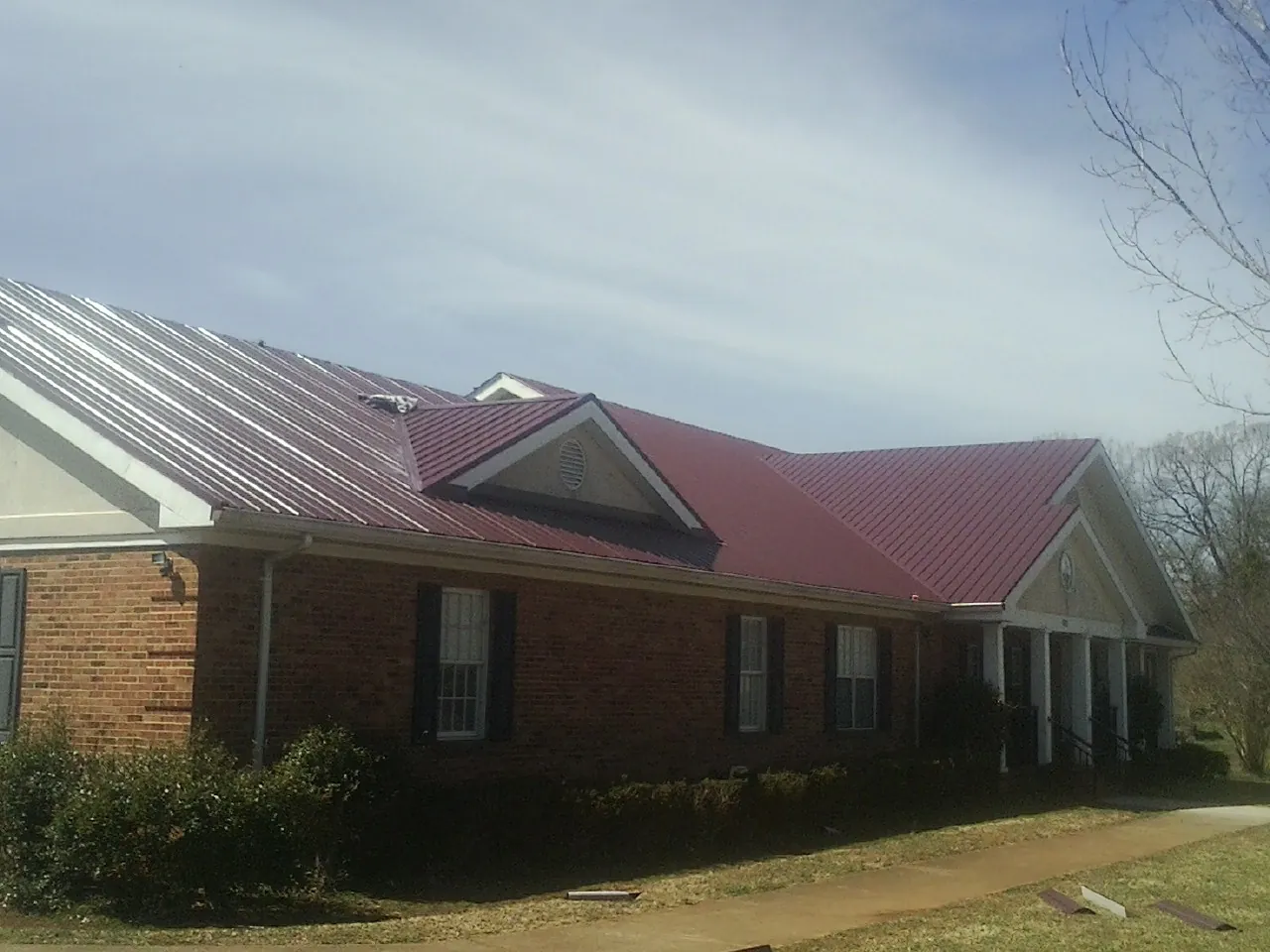 Red metal roof with gabled entries on a long brick building, from a Hail Damage Roof Repair job in Eminence