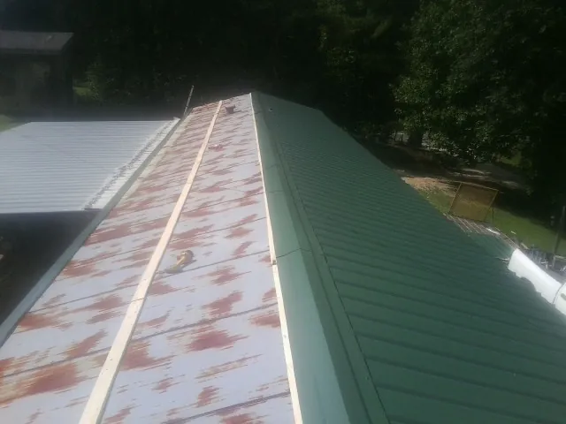 Old rusted panels beside newly installed green metal roofing — Wind Damage Roof Repair by Roofing Brothers in Eminence