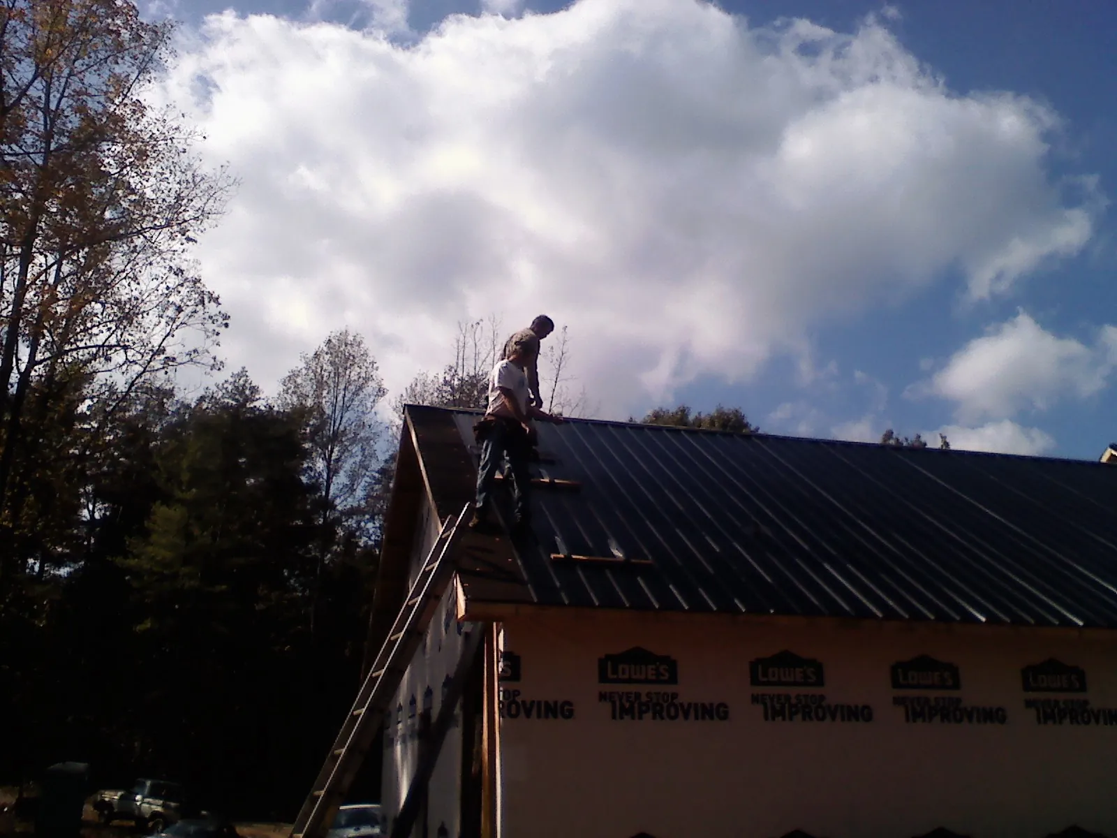 Roofer fastening dark metal panels high against a cloudy sky, from a Roof Inspection job in Eminence