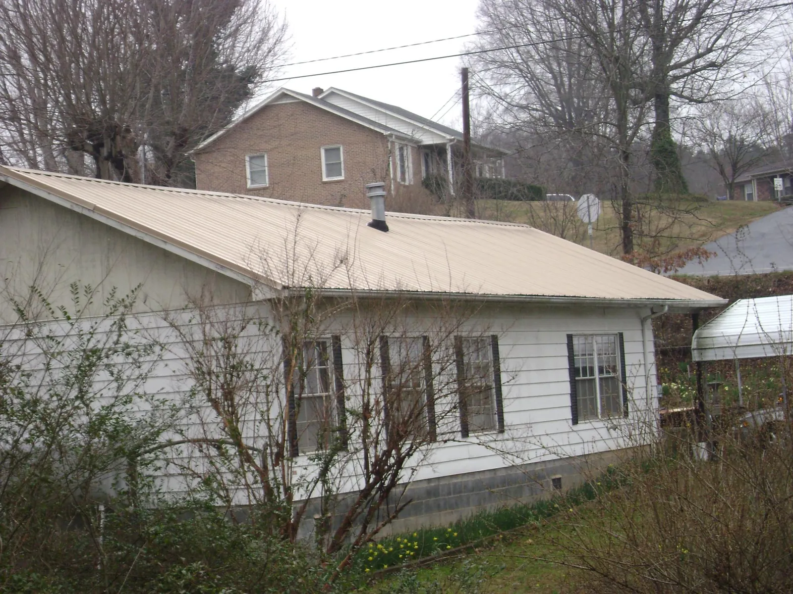 Tan metal roof on a white sided house set into a hillside — Commercial Roofing by Roofing Brothers in Eminence