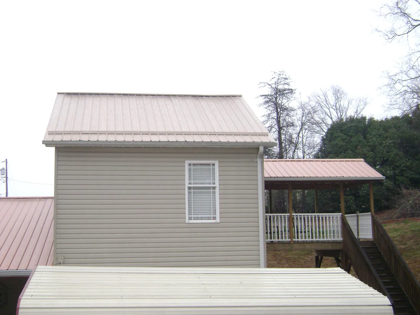 Tan metal roofs on a two story addition and attached porch, from a Roof Replacement job in Eminence